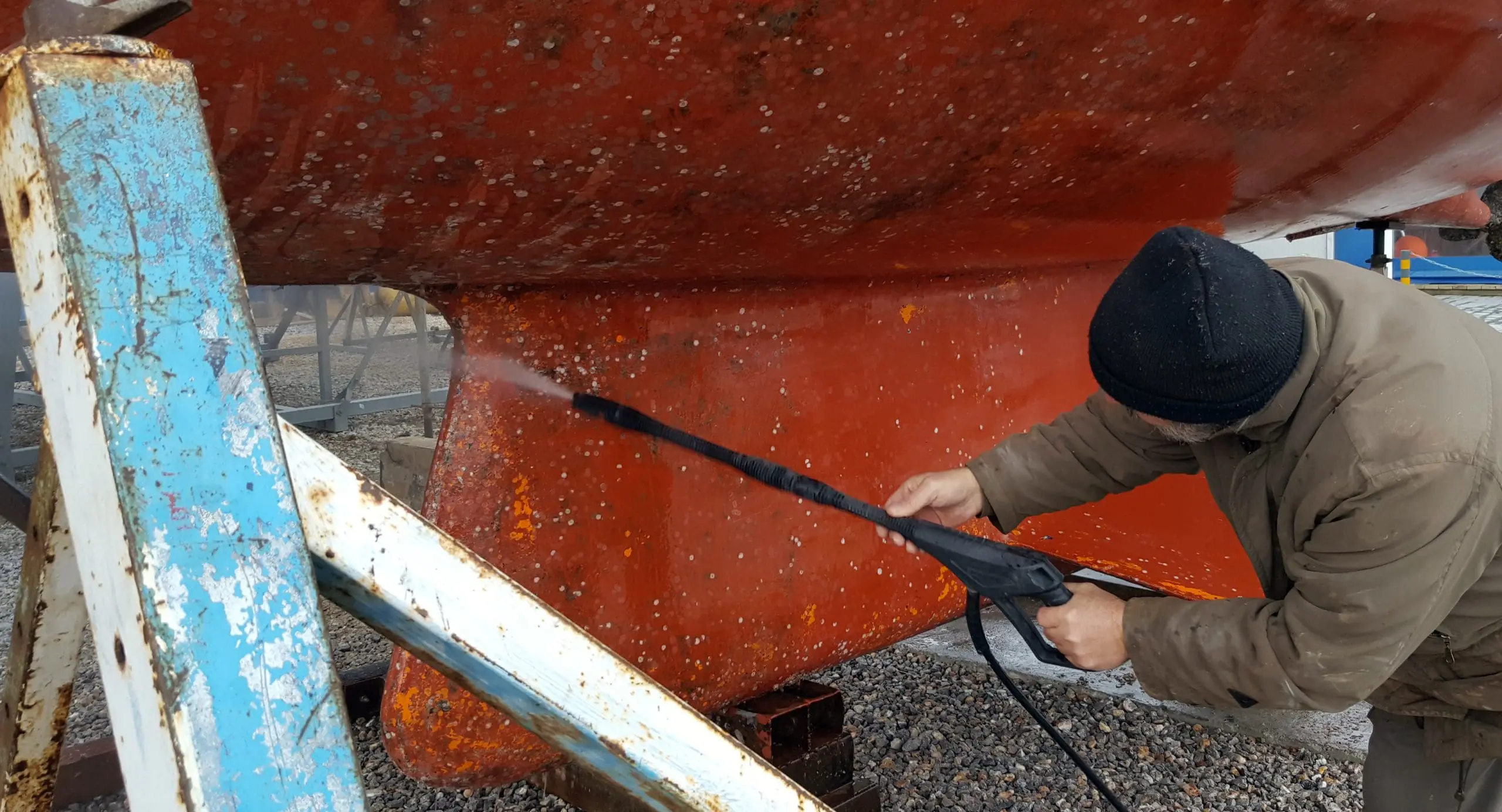 Man cleaning the bottom of a sailboat with high pressure water