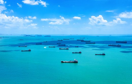 Aerial view of cargo, freight or container ships in the road in Singapore Strait. Blue sky, beautiful clouds, azure clear sea waters. Cargo ships anchored and waiting to enter the busiest port in South East Asia. Copyspace. International trade.